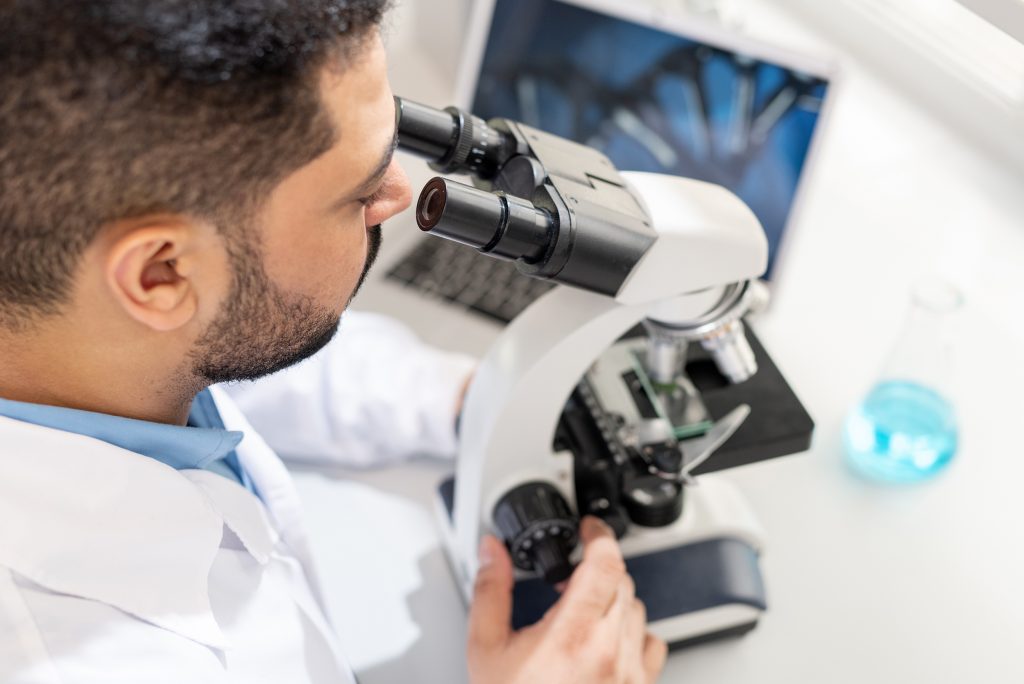 Pathologist looking into a microscope with laboratory informatics in the background.